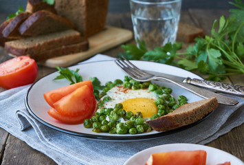 Fried egg with green peas and fresh tomatoes on a plate                     