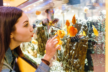 Smiling young brunette woman looking at fish in aquarium