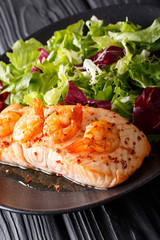 Baked salmon with prawns and honey sauce with a side dish of salad mix close-up on a plate. vertical