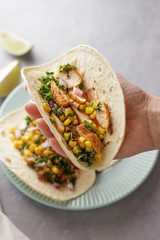 Hand holds mexican taco with chicken, corn, onion and parsley.