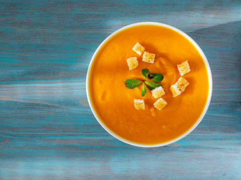 Big Bowl Of Pumpkin Soup On A Wooden Blue Background. Bright Tasty Dish, Top View