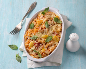 Baked pasta with tomato sauce, garlic, cheese and basil in white ceramic form on a light blue background. Delicious homemade food