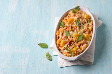 Baked pasta with tomato sauce, garlic, cheese and basil in white ceramic form on a light blue background. Delicious homemade food
