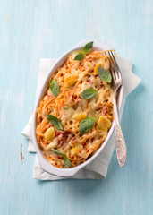 Baked pasta with tomato sauce, garlic, cheese and basil in white ceramic form on a light blue background. Delicious homemade food