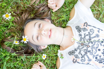 Relaxed young teenage girl lying in grass and flowers with stretched hand