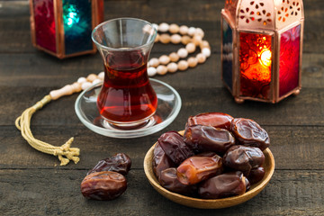 Ramadan Kareem Festive, close up of dates on wooden plate and rosary with oriental Lantern lamps and cup of black tea on wood background. Islamic Holy Month Greeting Card