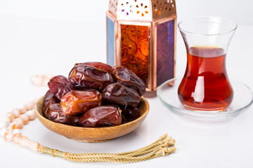 Ramadan Kareem Festive, close up of dates on wooden plate and rosary with oriental Lantern lamps and cup of black tea on white background. Islamic Holy Month Greeting