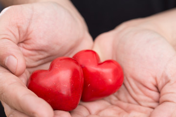 Male hands holding two red hearts, closeup background.