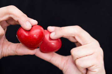 Male hands holding two red hearts, closeup on black background.