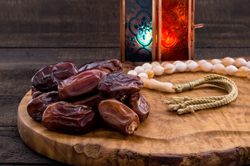 Close up of large premium dates on wooden board and rosary with oriental Lantern lamp on wood background. Islamic Holy Month Greeting Card, Ramadan Kareem