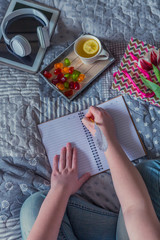 Naklejka na ściany i meble girl in jeans on a bed with tea with lemon a notebook and a tablet and a flower a tulip writes, the concept of coziness of philosophy kinkfolk and lagom and relaxation