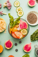 Top view of mixer with various healthy fruits and vegetables ingredients for tasty detox beverage or smoothie on light mint background. Dieting, clean eating and vegan concept