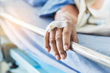 Close up hand of elderly patient with intravenous catheter for injection plug in the vein during lying in hospital ward room 
