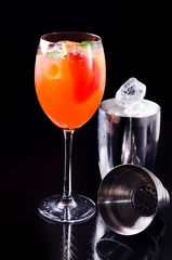Classic Italian Aperol Spritz cocktail with orange slice, fresh mint, fruit in wineglass and ice cube, shaker on bar, black background. Alcohol menu prosecco, aperitif and soda water, enjoy delicious.