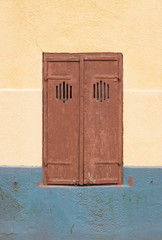 Old brown window blind on a yellow and blue wall