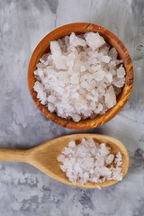 Large white sea salt in a natural wooden bowl on white background, top view, close-up, selective focus