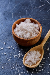 Large white sea salt in a natural wooden bowl on dark background, top view, close-up, selective focus