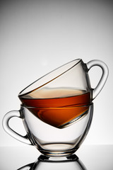 Conceptual composition of two glass teacups over colored light grey background, close-up, vertical.