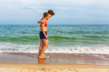 Two teenagers: a girl and a boy with blond hair, dressed in a swimsuit are walking on a sea beach. Copy space.