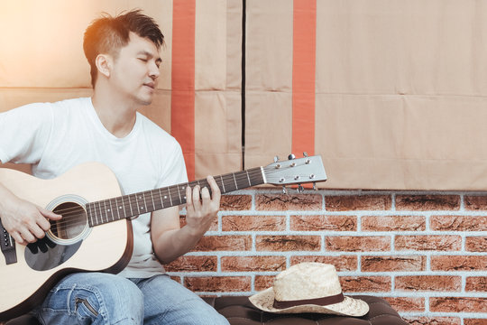 asian handsome man playing acoustic guitar on stool in loft design living room