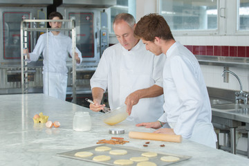 instructor and an apprentice in bakery making pretzels - obrazy, fototapety, plakaty