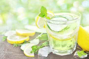 Cold summer cucumber lemonade on lemons background, glass of detox water, selective focus