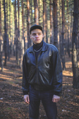A young man of criminal appearance in a black leather jacket posing in an autumn forest.