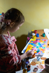 Cute little girl painting with paintbrush and colorful paints in home interior