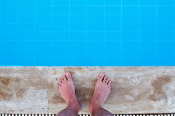 Men's legs on the edge of the pool with perfect blue water. Guy tourist on vacation, at the resort, in a luxury hotel with a swimming pool. The boy is preparing to jump into the cool water.