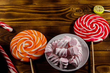 Colorful chocolate candies, lollipops, candy cane and marshmallows on wooden table