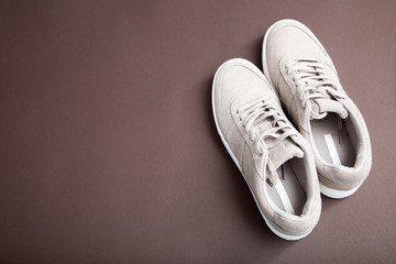 Pastel beige sneakers on a brown background. Flat lay, minimal background. Fashion blog or magazine concept..