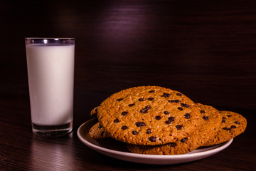 Plate with chocolate chip cookies and a glass of milk on a dark wooden table