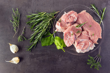 Fresh raw meat with herbs and spices  lies on the surface of a dark stone. Cooking concept.