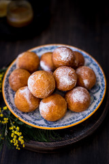 On a plate donuts with sugar powder, decorated with mimosa flowers. Wooden background