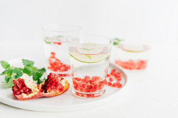 detox water in a glass with pomegranate seeds, mint leaves and lime on a white background, selective focus