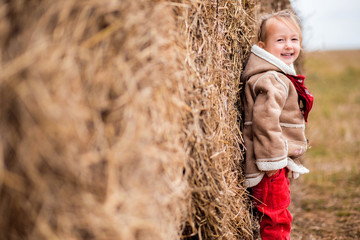 a little cheerful girl next to a haystack