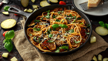 Vegetarian Italian Pasta Spaghetti alla Norma with eggplant, tomatoes, basil and parmesan cheese in rustic skillet pan. - obrazy, fototapety, plakaty