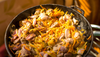 Cooked chicken hearts with onions and carrots in a frying pan.