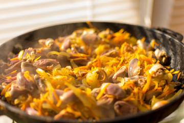 Cooked chicken hearts with onions and carrots in a frying pan.