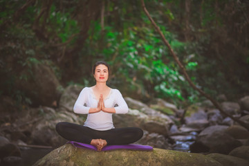 Young woman practicing yoga in rear view, waterfall