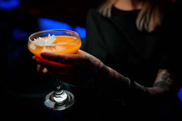 Orange cocktail in girls hands holing glass with tattoo