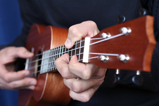 close up ukulele in musician hands, left hand view