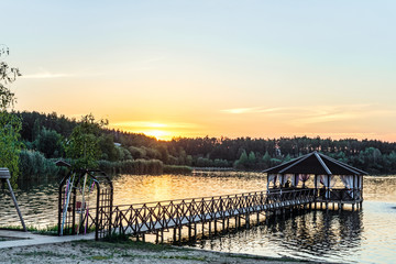 Footbridge with a gazebo on the lake shore in light of the low evening sun. Sunset and quiet...
