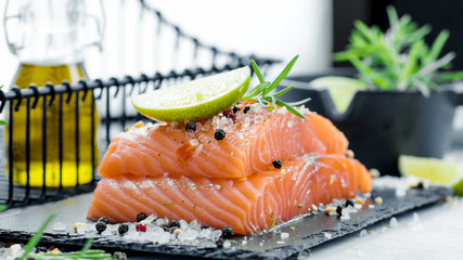 Two pieces of raw salmon fillet with fresh herb rosemary, spices and olive oil on black slate plate