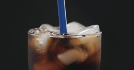 blue straw in cola with ice cubes in glass over black background