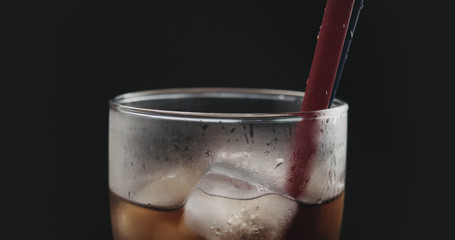 red straw in cola with ice cubes in glass over black background