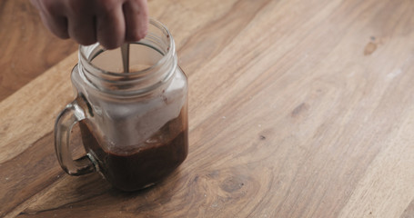 Obraz premium making cocoa drink in glass jar with handle on wood table, stirring cocoa
