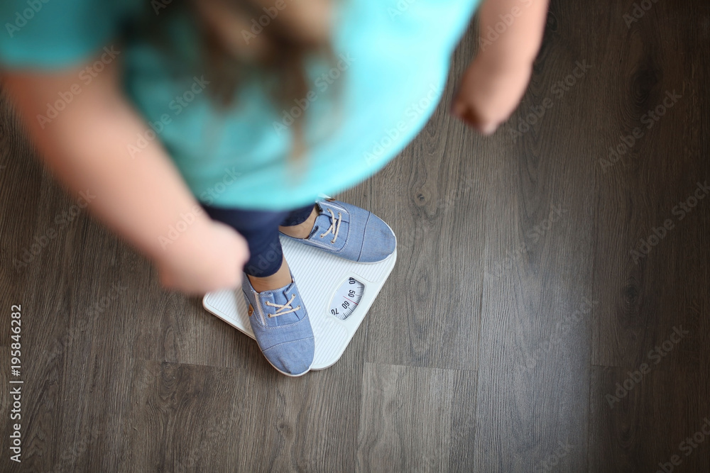 Wall mural overweight girl standing on floor scales indoors