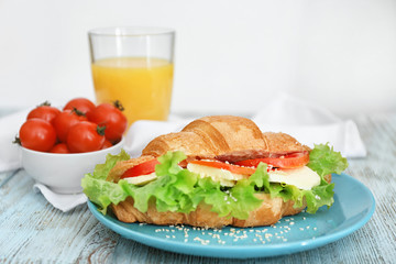 Plate with delicious croissant sandwich on wooden table