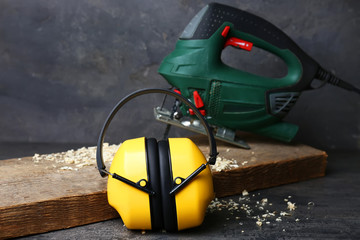 Headphones and electric jigsaw on background. Hearing protection equipment